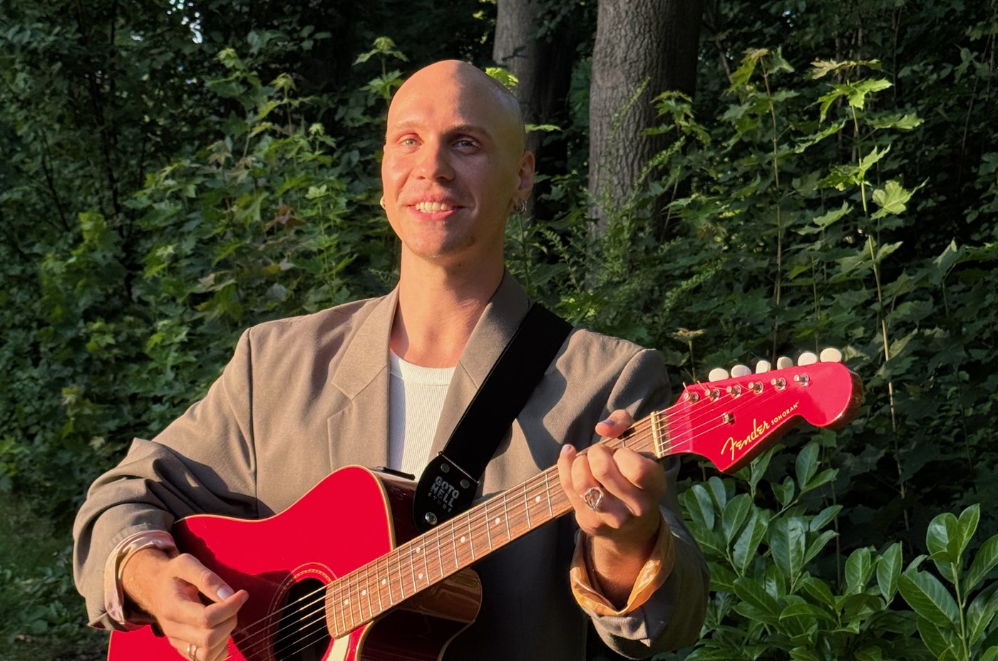 Paula spielt eine rote Gitarre, hinter ihr Büsche und Bäume in der Abendsonne